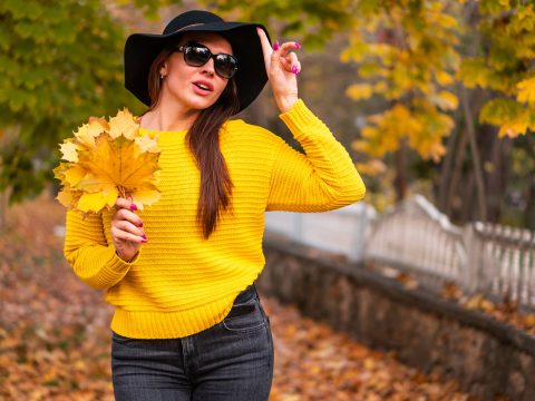 Femme en tenue chic d'automne tenant des feuilles jaunes