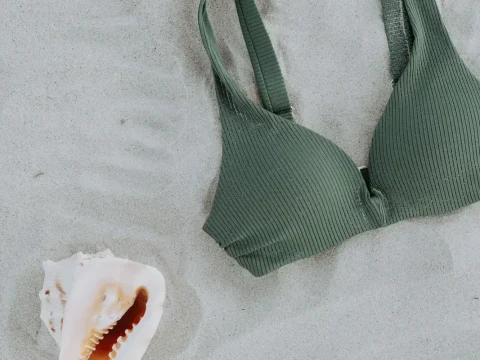 Haut de maillot de bain vert posé sur le sable à côté d’un coquillage