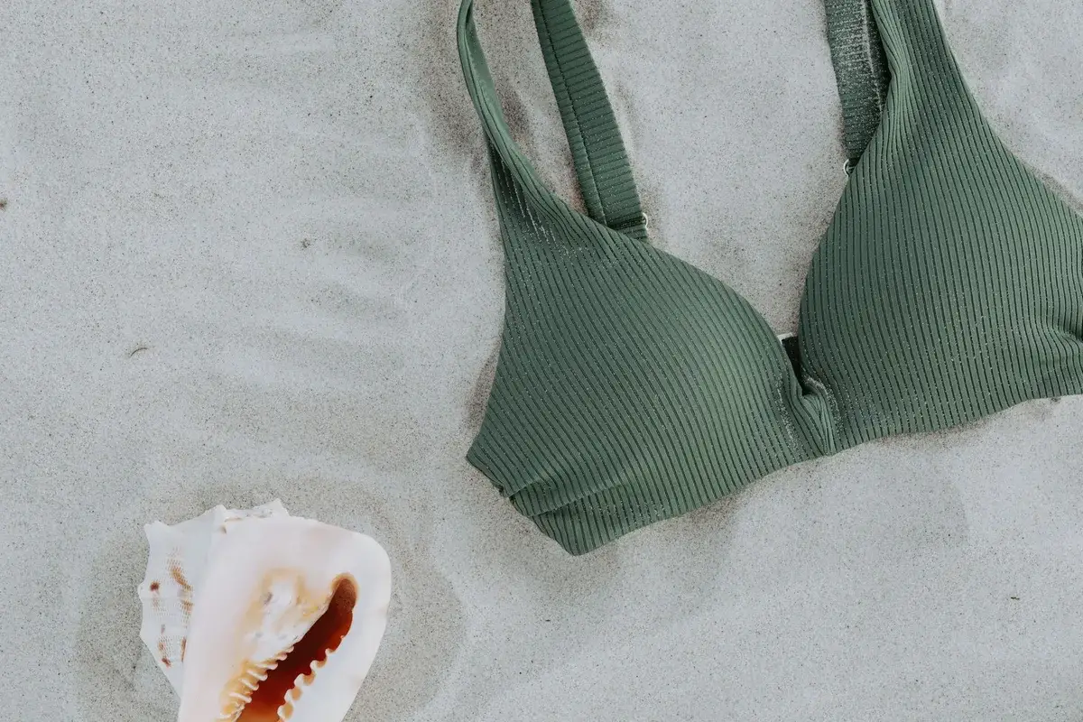 Haut de maillot de bain vert posé sur le sable à côté d’un coquillage