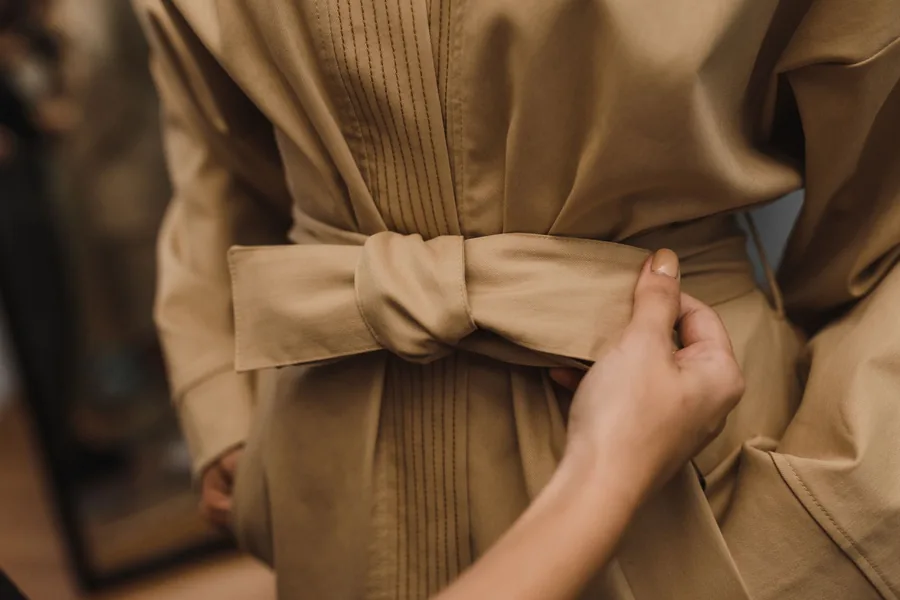 Mains nouant la ceinture d'un trench beige