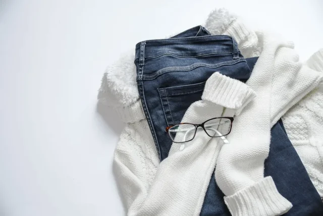 Jean, maille blanche et paire de lunettes posés à plat sur fond clair