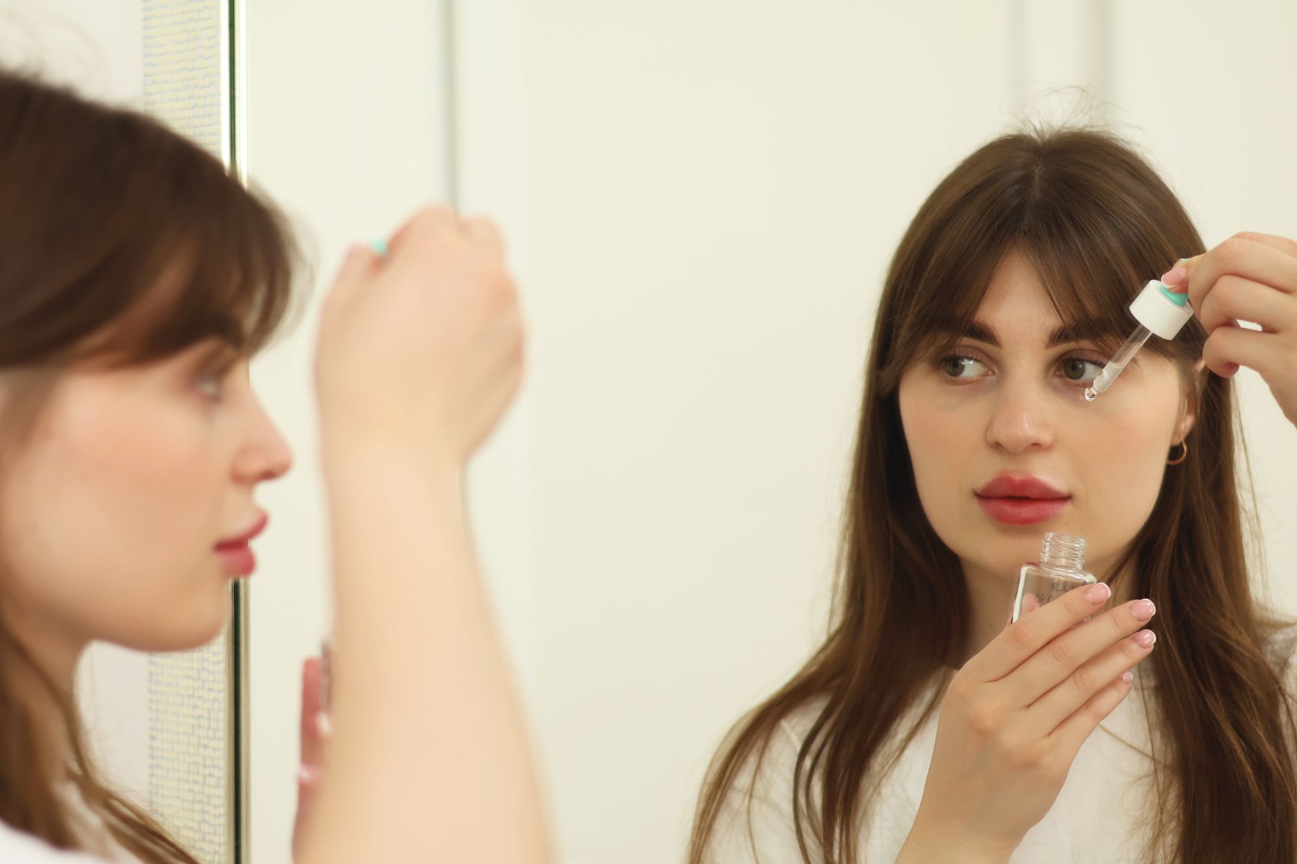 jeune femme qui applique un sérum devant un miroir dans le cadre d'une routine de soin du visage