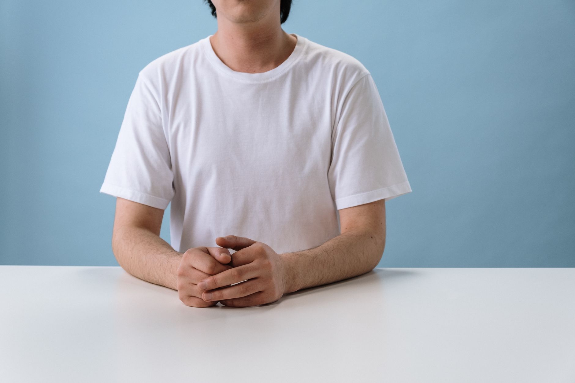 Homme assis à une table, mains posées devant lui, portant un t-shirt blanc uni en coton
