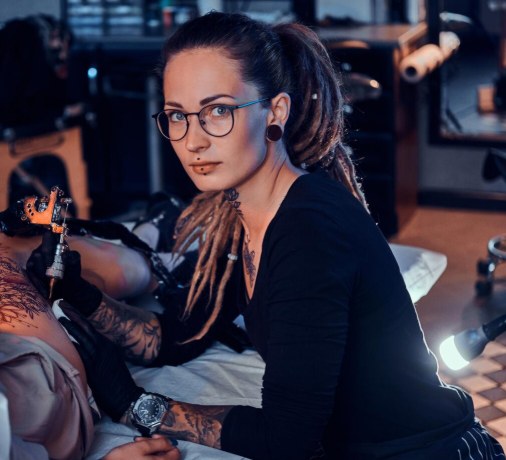 Tatoueuse indépendante au travail, concentrée sur une cliente en studio